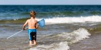 dreng med fiskenet på vej ud i bølgerne ved stranden 